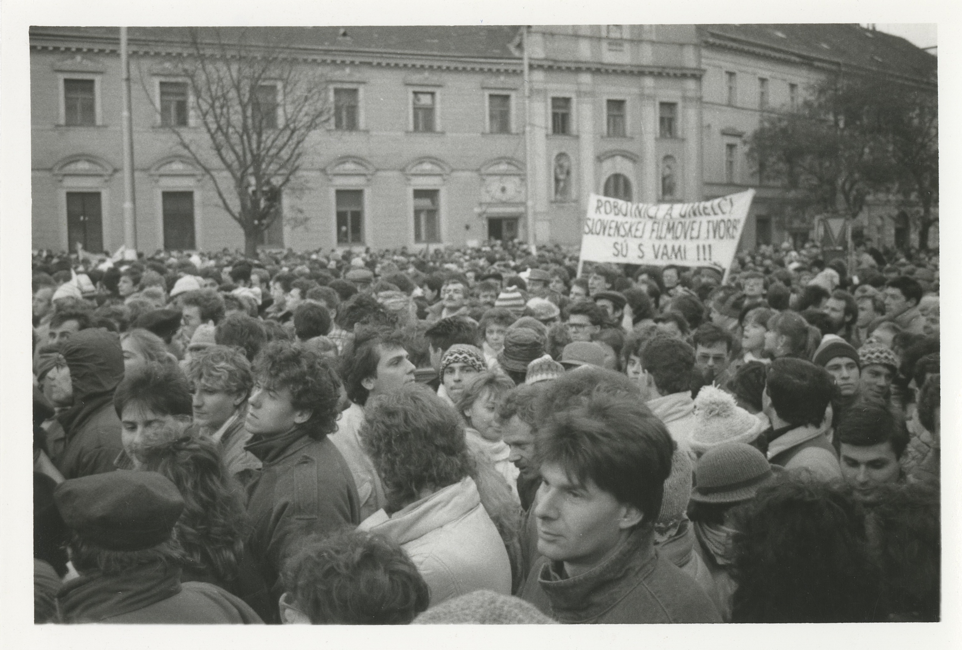 : pos/68370/019: Menschenmenge auf dem Námestie SNP. Banner: “ROBOTNICI A UMELCI SLOVENSKEJ FILMOVEJ TVORBY SÚ S VAMI !!!” [ARBEITER UND KÜNSTLER DER SLOWAKISCHEN FILMPRODUKTION SIND MIT EUCH !!!] (zeigt Menschen und Banner gleichermaßen plus Gebäude in Bratislava). Foto: Helena Bakaljarova 